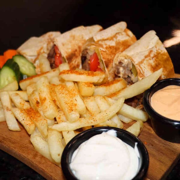 Shawarma Box shawarmas, seasoned fries, cucumber, carrots, and two dipping sauces on a wooden board.