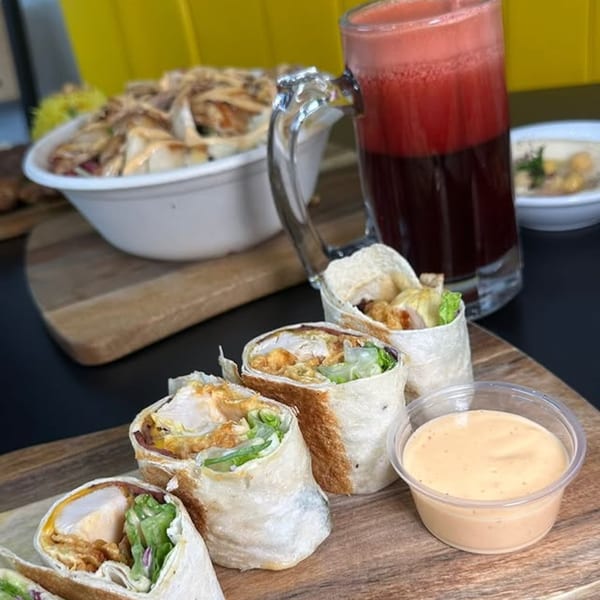 Shawarma Box chicken shawarma wraps, a bowl of chicken, a red drink, and hummus on a wooden board.
