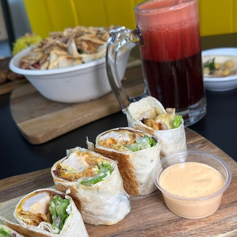 Shawarma Box chicken shawarma wraps, a bowl of chicken, a red drink, and hummus on a wooden board.