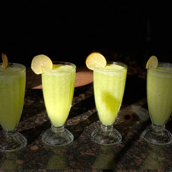 Four glasses of refreshing green lemonade with lemon slices on a dark, reflective surface.