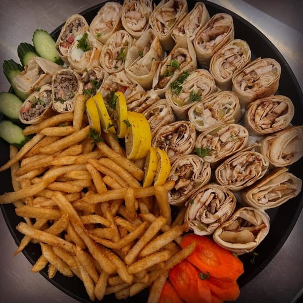 A platter of Shawarma Box wraps, french fries, cucumber slices, and lemon wedges.