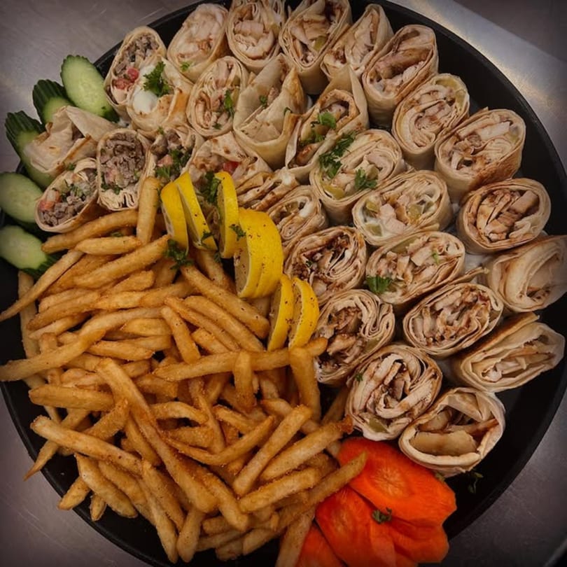 A platter of Shawarma Box wraps, french fries, cucumber slices, and lemon wedges.