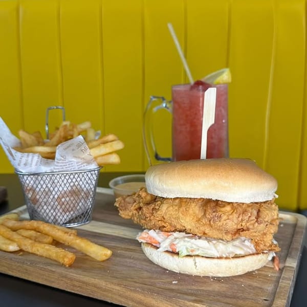 Crispy chicken sandwich with coleslaw, fries in a basket, and a red drink on a wooden tray.