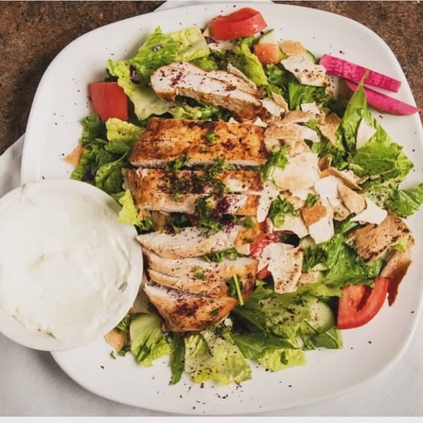 Shawarma Box's chicken shawarma salad with lettuce, tomatoes, pita, and a side of white sauce.