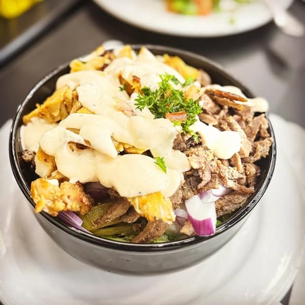 Shawarma Box's Mediterranean bowl with meat, fries, red onions, and a creamy white sauce, garnished with parsley.