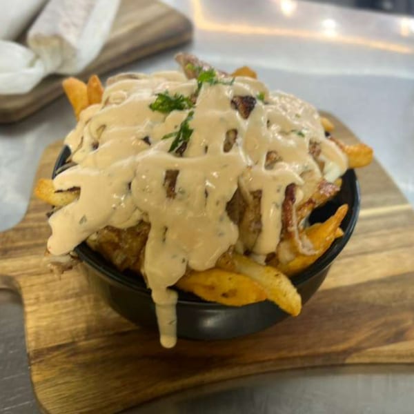 Shawarma Box's shawarma fries, topped with creamy sauce and fresh parsley, served in a black bowl.